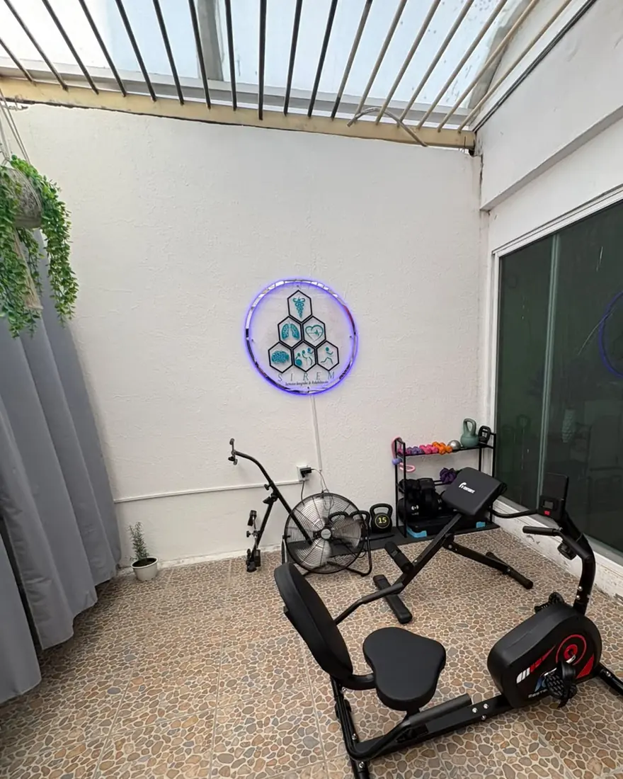 Área de ejercicio terapéutico de SIREM con bicicleta reclinada, pesas y el logotipo iluminado
